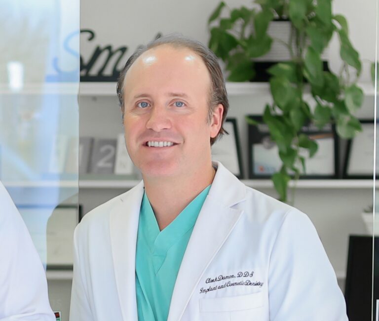 Dr. Clark Damon standing in a white coat with green scrubs