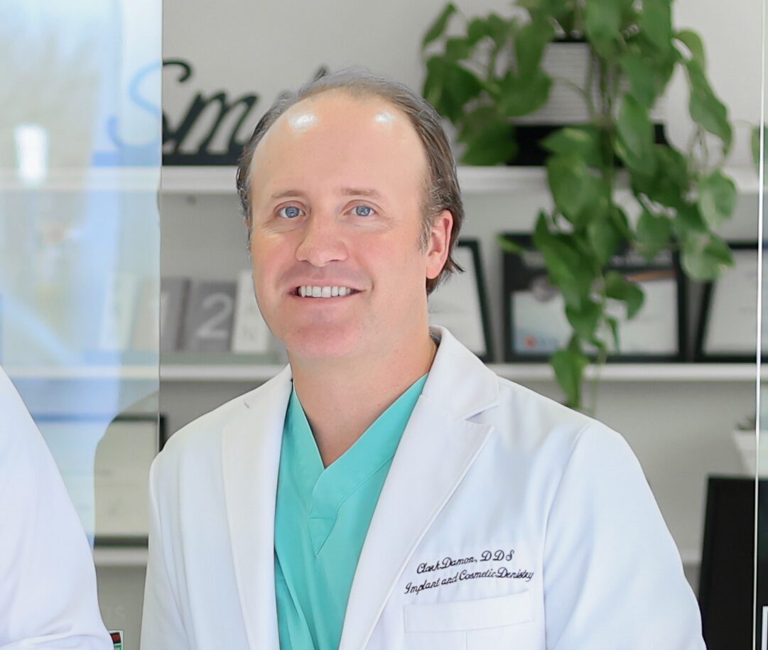 Dr. Clark Damon standing in a white coat with green scrubs